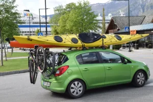 En grønn kombibil med to sykler festet bak og to gule kajakker festet på taket, parkert utendørs i et fjellområde – en sann scene fra Eidfjord, hvor sport og fritid blomstrer i Norsk natur.